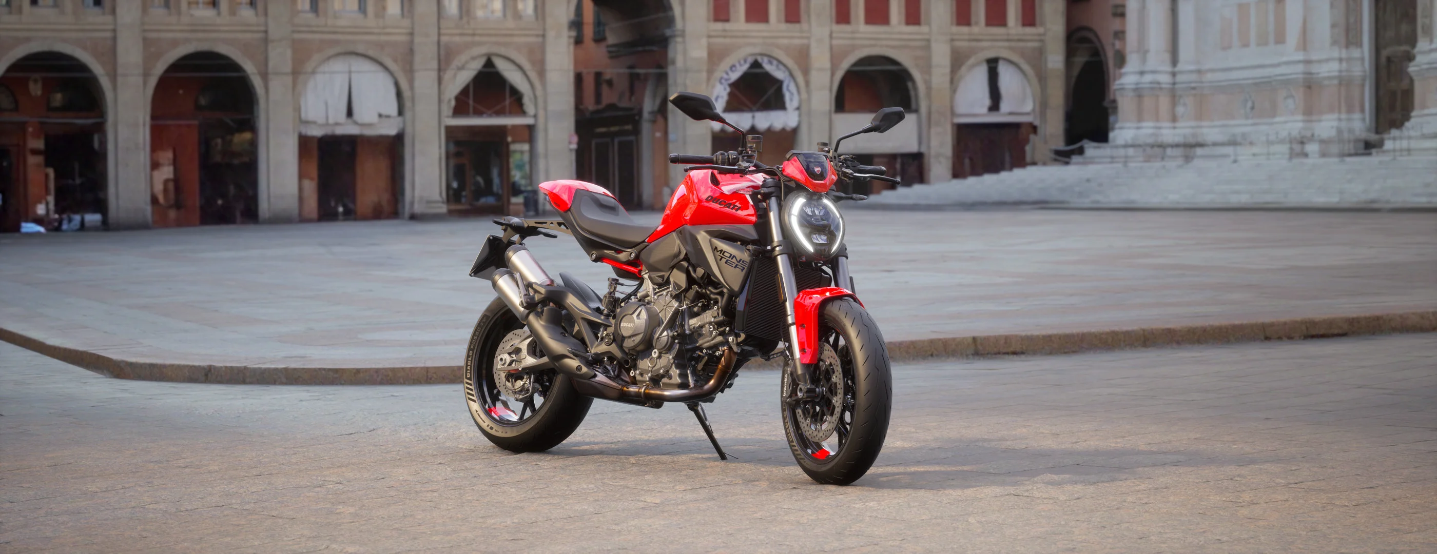 2026 Ducati Monster+ red front three-quarter view in an urban plaza